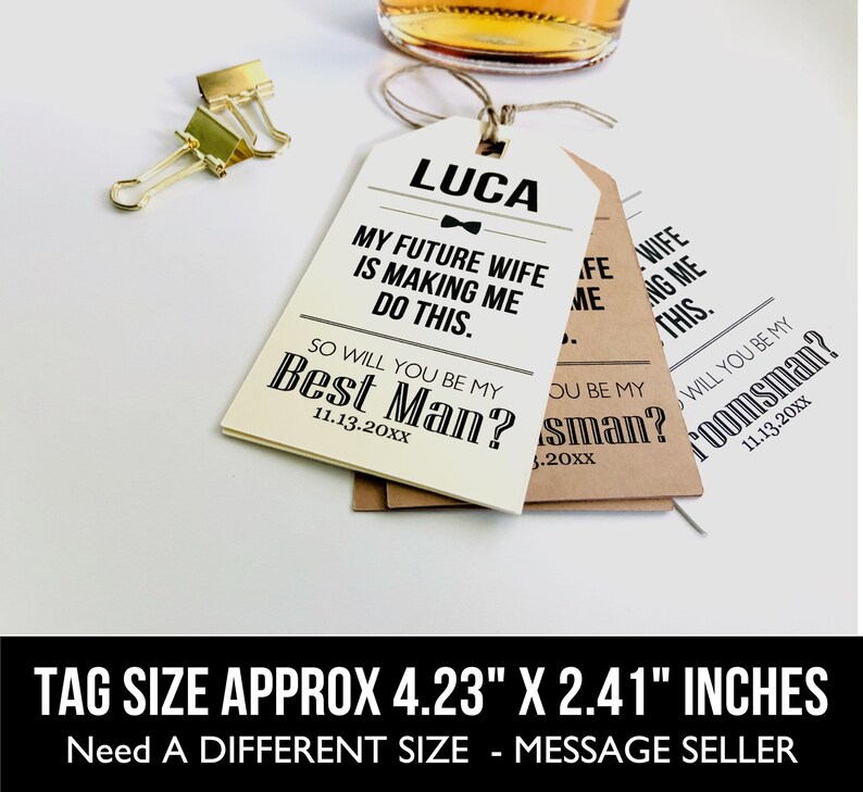 May include: Two white and brown gift tags with black text. The text on the white tag reads "LUCA MY FUTURE WIFE IS MAKING ME DO THIS. SO WILL YOU BE MY BEST MAN? 11.13.20XX". The text on the brown tag reads "WILL YOU BE MY GROOMSMAN? 11.13.20XX". The tags are approximately 4.23 inches by 2.41 inches.