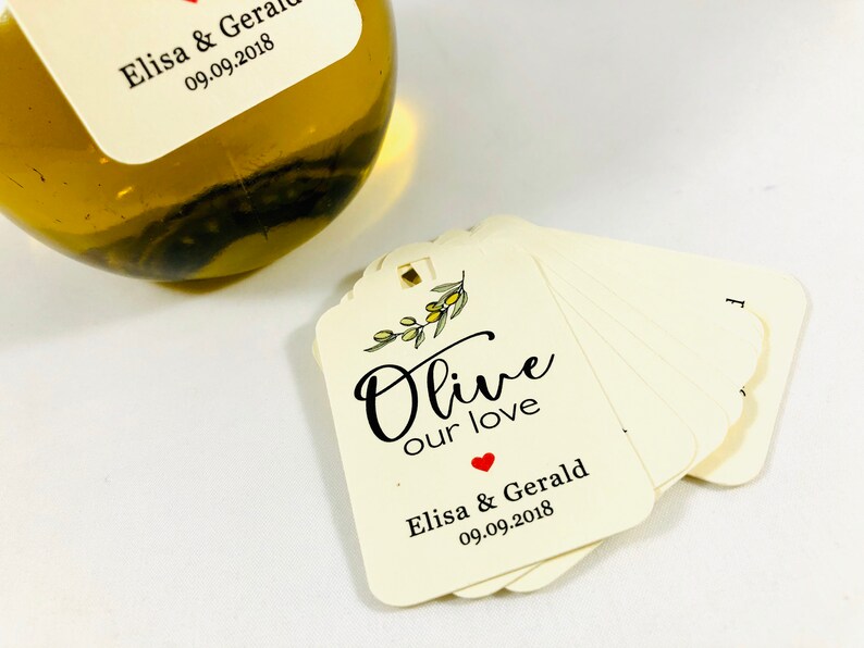 May include: A stack of ivory-colored gift tags with a small olive branch illustration and the text "Olive our love" in black script. The bottom tag has the text "Elisa & Gerald 09.09.2018" in black text with a small red heart.