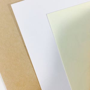 May include: Three sheets of paper stacked on top of each other. The bottom sheet is brown, the middle sheet is white, and the top sheet is a light yellow.