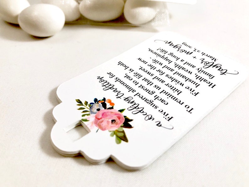 Puede incluir: Etiqueta de favor blanca con un dise&ntilde;o floral y el texto "a Wedding tradition Five sugared almonds for each guest to eat, bitter and sweet. To remind us that life is both Five wishes for the new husband and wife - Health, wealth, happiness, family and a long life! taylor + morgan 23, 2019"