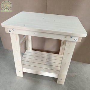 May include: A natural wood workbench with a single shelf. The workbench is made of unfinished pine wood and has a simple design.