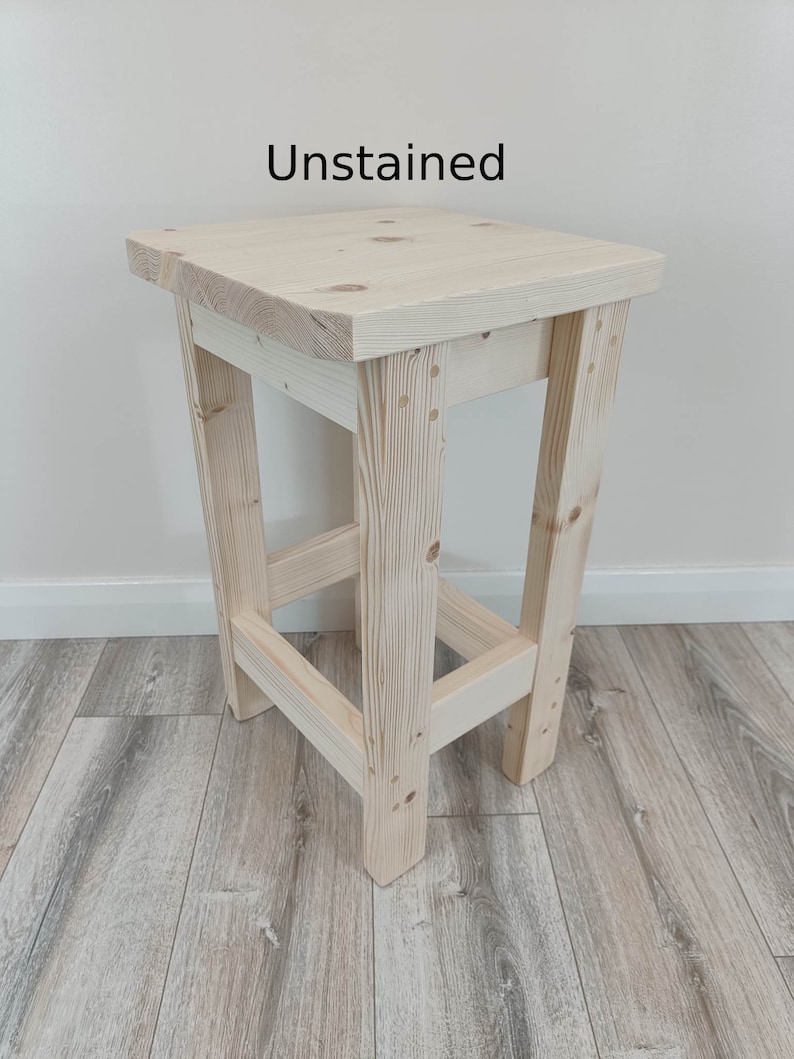 K&ouml;nnte beinhalten: Ein unbehandelter Holzstuhl mit quadratischer Sitzfl&auml;che und vier abgewinkelten Beinen. Der Text "Unstained" ist auf der Oberseite aufgedruckt. Der Hocker besteht aus Naturholz und weist sichtbare Maserungen auf. Die H&ouml;he betr&auml;gt ca. 76 cm.