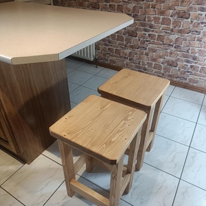 K&ouml;nnte beinhalten: Zwei Holzst&uuml;hle mit nat&uuml;rlicher Oberfl&auml;che. Die Hocker haben eine quadratische Sitzfl&auml;che und vier stabile Beine. Die Holzmaserung ist sichtbar, was ihnen ein rustikales Aussehen verleiht. Sie stehen vor einer K&uuml;chenzeile.