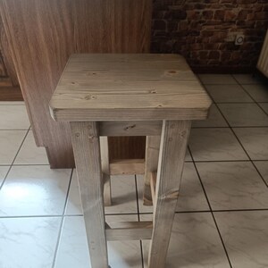 K&ouml;nnte beinhalten: Ein rustikaler, hell get&ouml;nter Holzstuhl mit quadratischer Sitzfl&auml;che und vier stabilen Beinen. Der Hocker ist mit sichtbarer Holzmaserung und Verbindungen versehen und zeigt eine nat&uuml;rliche, unbehandelte &Auml;sthetik. Ideal f&uuml;r K&uuml;chen oder Barbereiche.
