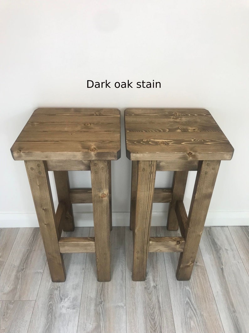 K&ouml;nnte beinhalten: Zwei Barhocker aus Holz mit dunkler Eichenbeize. Jeder Hocker hat eine quadratische Sitzfl&auml;che und vier stabile Beine. Der Text "Dark oak stain" steht &uuml;ber den Hockern.