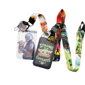 Puede incluir: Dos cordones de Star Wars con portatarjetas. Un portatarjetas muestra a The Mandalorian y Grogu, el otro tiene un fondo negro con Grogu y el texto Strong in me cuteness is. Los cordones están impresos con gráficos coloridos de personajes.