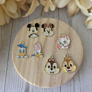 May include: A collection of seven metal enamel charms featuring cartoon characters including Mickey Mouse, Minnie Mouse, Marie the cat, Donald Duck, Daisy Duck, Chip, and Dale. Each charm has a small metal loop at the top for attachment.
