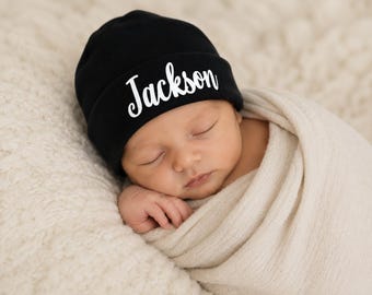 Könnte beinhalten: Eine einfarbige schwarze Neugeborenenmütze mit dem Namen Jackson, der in weißer Schreibschrift auf dem vorderen Umschlag aufgedruckt ist. Die Mütze besteht aus weichem Stoff und ist so konzipiert, dass sie eng am Kopf eines Säuglings anliegt.