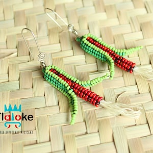 May include: A pair of handmade earrings featuring a red and green beaded design resembling corn on the cob. The earrings have a silver wire hook and a white tassel.