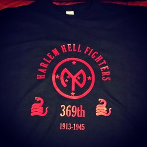 May include: Black t-shirt with a red circle logo that says "Harlem Hell Fighters" and a red "369th" with the years "1913-1945" below it.
