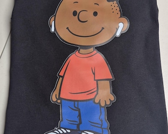 May include: Black t-shirt featuring a cartoon illustration of a smiling boy wearing earbuds. The boy is depicted in a red shirt, blue jeans, and black and white sneakers. The graphic is centered on the shirt.
