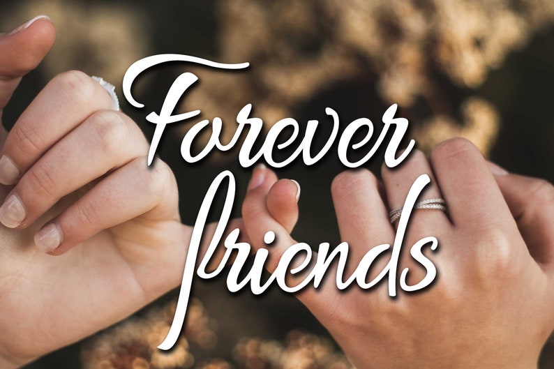 May include: Image shows two hands clasped together, with fingers interlocked. The text "Forever friends" is written in a cursive font over the hands. Both hands have rings on the ring fingers. The background is blurred.