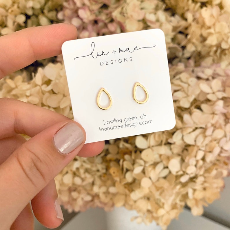 May include: Gold teardrop shaped earrings on a white card with the text "lin + mae DESIGNS" and "bowling green, oh linandmaedesigns.com"