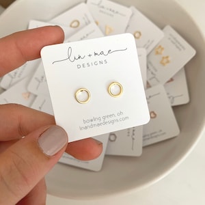 May include: A pair of gold hoop earrings on a white card with the text "lin + mae DESIGNS" and "bowling green, oh linandmaedesigns.com".