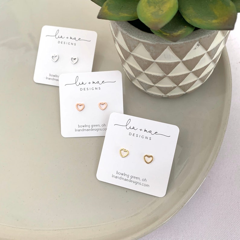 May include: Three cards with the text "lin+mac DESIGNS" on them. Each card has two small heart-shaped earrings on them. The earrings are in silver, rose gold, and gold.
