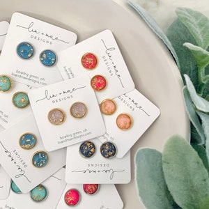 May include: Assortment of handmade resin earrings with gold flakes. The earrings are displayed on white cards with the text "lin+mac DESIGNS" and the website address "linandmaedesigns.com".