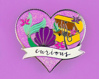 May include: A heart-shaped enamel pin with a purple seashell, a green mermaid tail, a yellow treasure chest, and a fork. The pin has a sparkly pink background and the word "curious" written on a white banner.