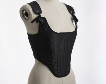 May include: A black corset with a square neckline and adjustable straps. The corset has a boned structure and is made of a smooth fabric.