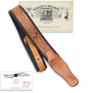 May include: A brown and black leather guitar strap with embossed floral designs. The strap has a light brown shoulder pad and a buckle for adjustment. The image includes the text "WALKER & WILLIAMS" and "GB-104 LATIGO TAN LIVE OAK".