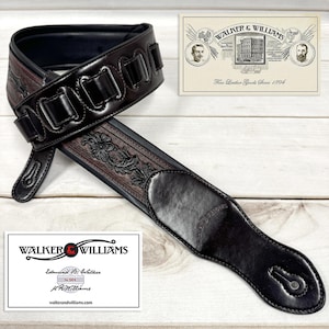 May include: A brown leather guitar strap with a black leather trim and embossed floral design. The strap has a buckle and a strap keeper. The strap is made by Walker & Williams, a company that has been making fine leather goods since 1894.
