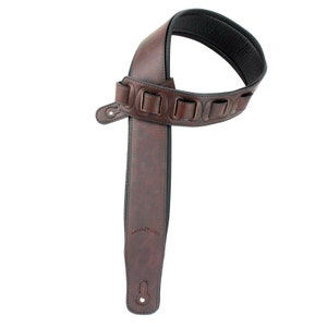 Puede incluir: Una correa de guitarra de cuero marr&oacute;n con costuras decorativas y una hebilla. La correa tiene un extremo de cuero marr&oacute;n con un bot&oacute;n de metal.