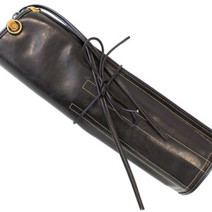 May include: A black leather roll-up case with a yellow stitching detail and a brown leather strap with a metal buckle.