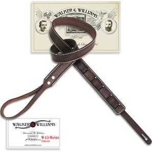 May include: A dark brown leather guitar strap with white stitching and a padded shoulder section. The strap has the text "WALKER & WILLIAMS" and "M-13-MANDO" on a tag.