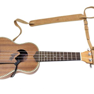 Peut inclure: Un ukul&eacute;l&eacute; brun avec une sangle en cuir attach&eacute;e &agrave; la t&ecirc;te. La sangle est brune et porte un petit cercle avec le texte "Music Street".