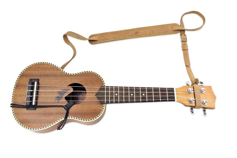 Peut inclure: Un ukul&eacute;l&eacute; brun avec une sangle en cuir attach&eacute;e &agrave; la t&ecirc;te. La sangle est brune et porte un petit cercle avec le texte "Music Street".