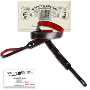 May include: Black leather guitar strap with red stitching. The strap has a buckle and a length adjustment system. The strap is labeled "M-12 Black & Scarlet".