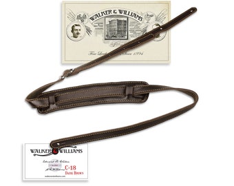 May include: Dark brown leather guitar strap with yellow stitching. The strap has a padded shoulder section and a metal buckle. The image includes a tag that reads "WALKER & WILLIAMS" and "C-18 DARK BROWN".