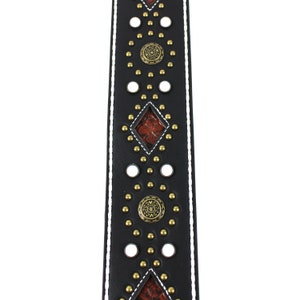 Pu&ograve; includere: Cinturino per chitarra in pelle nera con cuciture bianche e borchie e dettagli dorati. Il cinturino ha un motivo a forma di diamante con un inserto in pelle marrone.