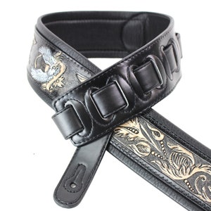 May include: Black leather guitar strap with gold and silver floral embroidery. The strap has a padded section and adjustable length.