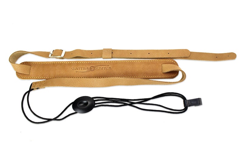 Peut inclure: Sangle de guitare en cuir beige avec une boucle et un verrou de sangle noir. La sangle porte le texte "Walter Williams" en relief.