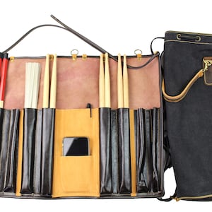 May include: A brown leather drum stick bag with multiple pockets for storing drumsticks, brushes, and a phone. The bag has a black canvas carrying case with a drawstring closure.