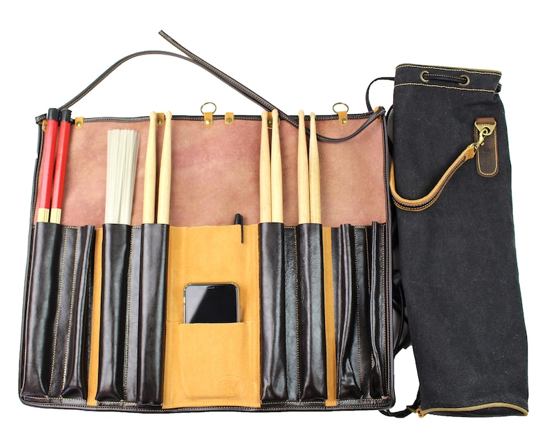 May include: A brown leather drum stick bag with multiple pockets for storing drumsticks, brushes, and a phone. The bag has a black canvas carrying case with a drawstring closure.