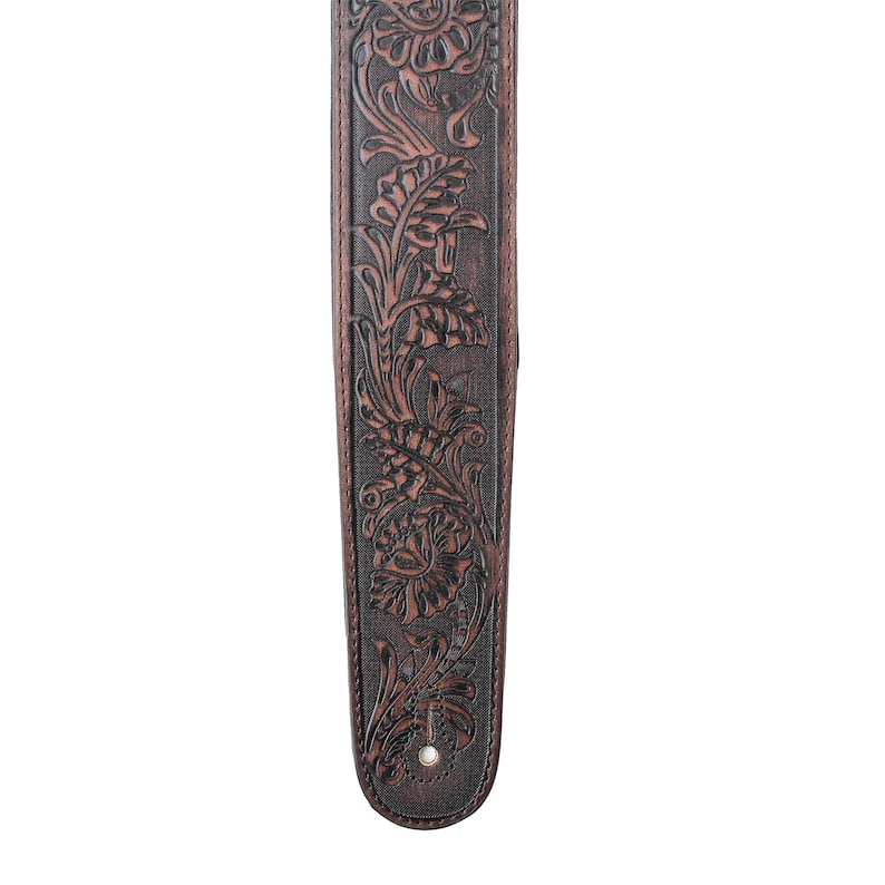 Puede incluir: Una correa de guitarra de cuero marr&oacute;n con un dise&ntilde;o floral en relieve.