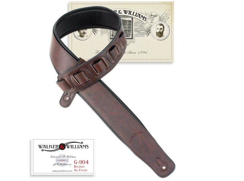 Puede incluir: Correa de guitarra de cuero marr&oacute;n con un patr&oacute;n decorativo y una parte inferior acolchada negra. La correa est&aacute; etiquetada "G-904 Bourbon Oil Finish" y "Walker & Williams Established 1894".