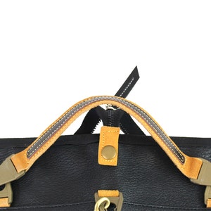 May include: Close-up of a black leather bag with a tan leather handle and a zipper closure. The handle has a brown stitching detail.