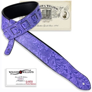 May include: Purple leather guitar strap with a paisley pattern and black edging. The strap has two adjustable straps and a Walker & Williams logo tag. The tag reads "Walker & Williams, Established 1894, G-972 Purple Sheridan, walkerandwilliams.com".