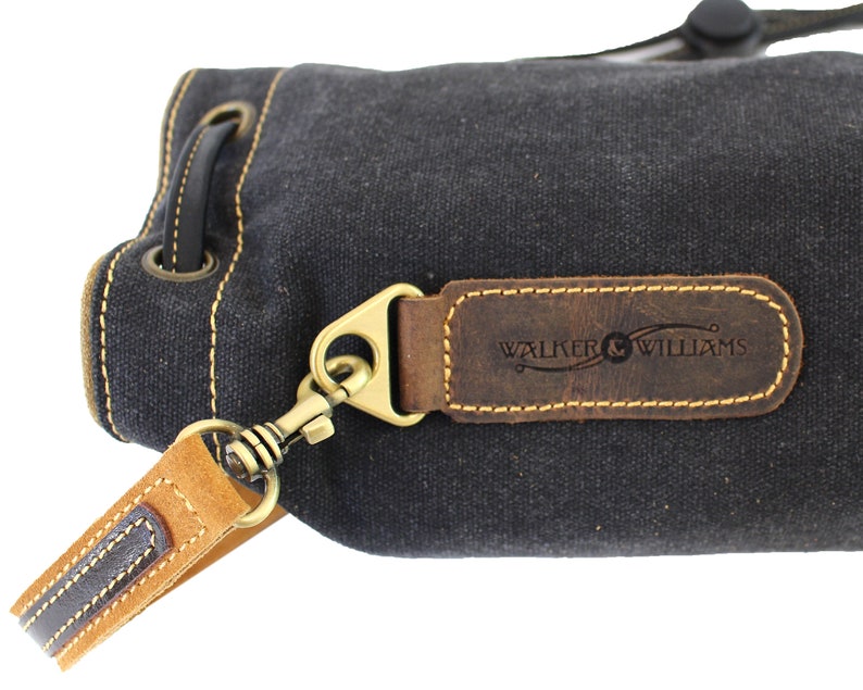 May include: A black canvas drawstring bag with a brown leather strap and a brown leather patch with the text "WALKER & WILLIAMS" embossed on it.