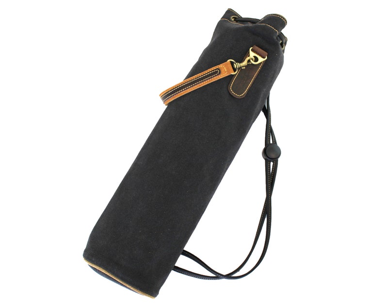 May include: A black canvas drawstring bag with a brown leather strap and a brass buckle. The bag has a black drawstring closure and a black strap with a black plastic buckle.