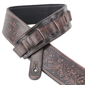 Puede incluir: Correa de guitarra de cuero marr&oacute;n con un dise&ntilde;o floral en relieve y hebilla ajustable.