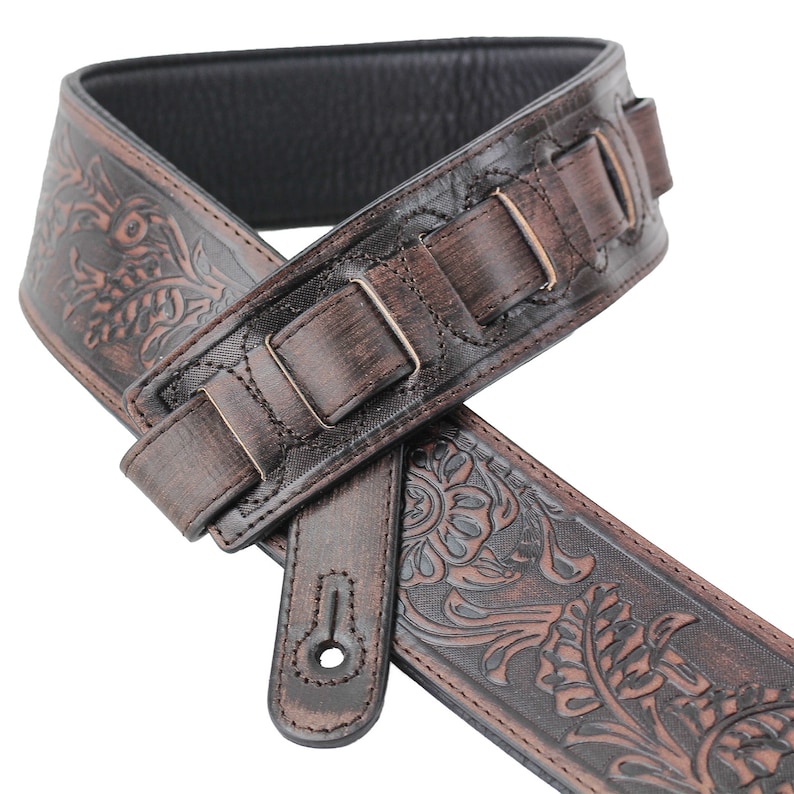 Puede incluir: Correa de guitarra de cuero marr&oacute;n con un dise&ntilde;o floral en relieve y hebilla ajustable.