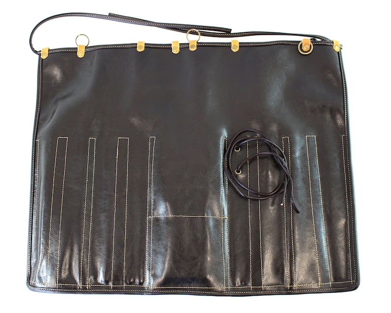 May include: A black leather roll with multiple slots for holding tools or utensils. The roll has a strap with a buckle and gold metal accents.