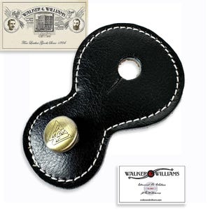 May include: Black leather strap with a white stitched edge and a brass button with a logo. The strap has a hole in the center and is shaped like a figure eight.