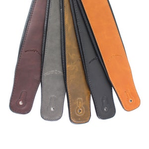 Puede incluir: Seis correas de guitarra de cuero en diferentes colores, incluyendo marr&oacute;n, gris, marr&oacute;n claro y negro. Cada correa tiene las palabras "Water Buffalo" grabadas.