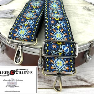 May include: A blue and orange patterned guitar strap with a black background. The strap has two metal clasps and is shown on a banjo.
