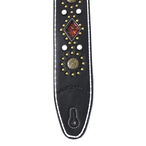 Pu&ograve; includere: Cinturino per chitarra in pelle nera con cuciture bianche e borchie e dettagli dorati. Il cinturino presenta un intarsio a forma di diamante con un motivo rosso e marrone. Il cinturino &egrave; marchiato "Fender Williams".