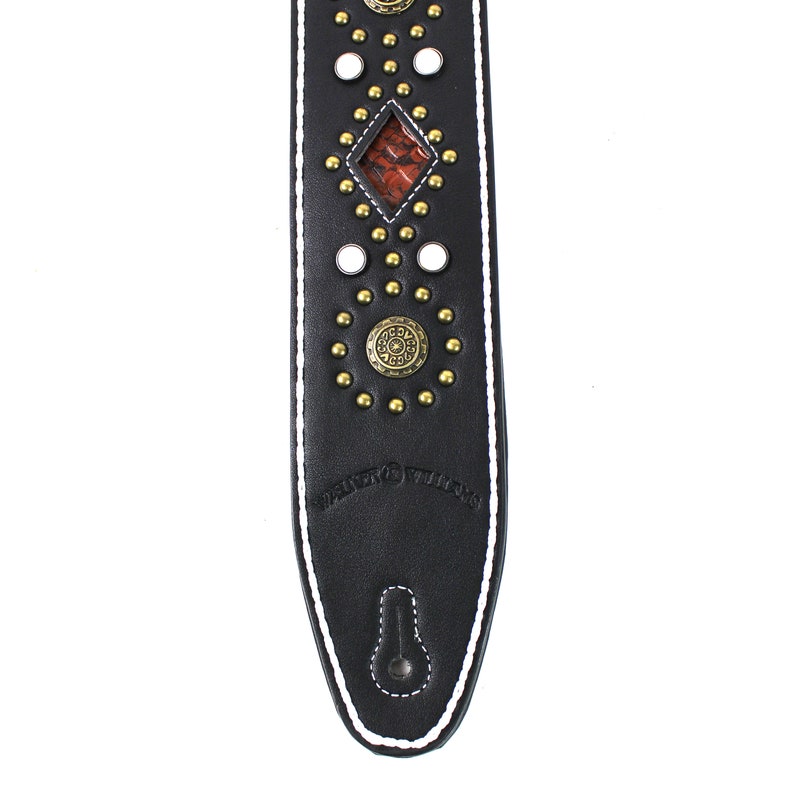 Pu&ograve; includere: Cinturino per chitarra in pelle nera con cuciture bianche e borchie e dettagli dorati. Il cinturino presenta un intarsio a forma di diamante con un motivo rosso e marrone. Il cinturino &egrave; marchiato "Fender Williams".